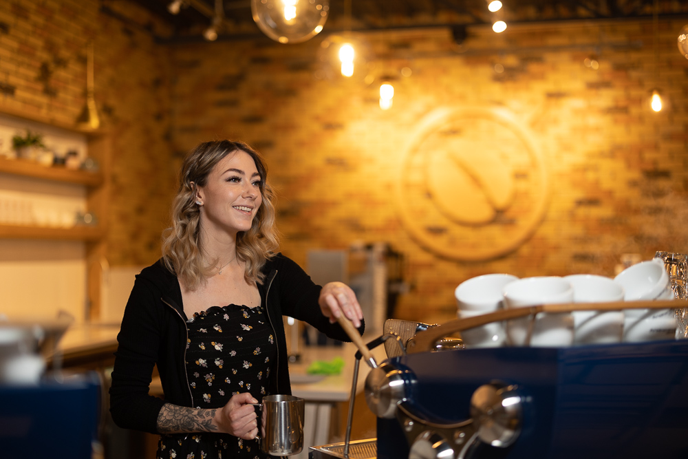 A barista at Snowdome Coffee Bar serving a cup of coffee to a happy customer